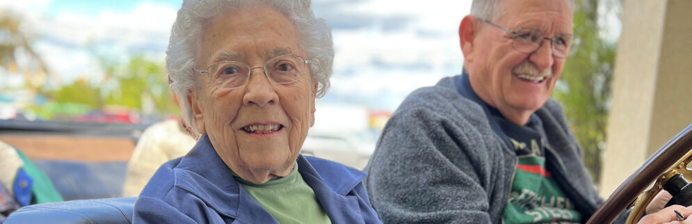 an elderly woman smiles while sitting next to an older man