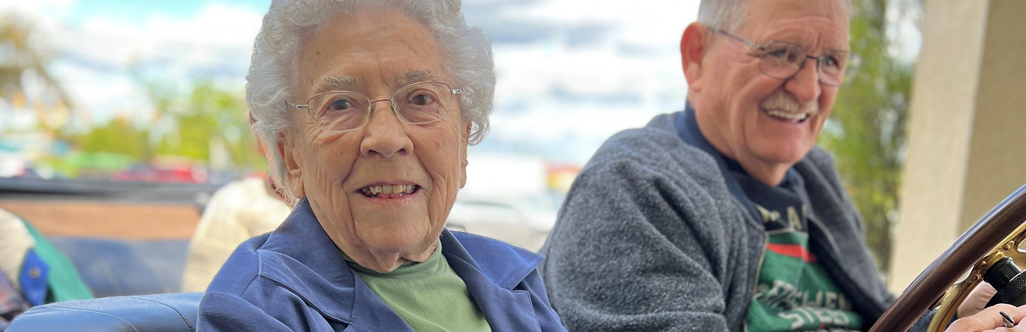 an elderly woman smiles while sitting next to an older man