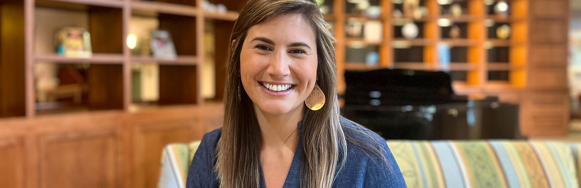 a woman wearing a blue shirt and gold earrings smiles for the camera