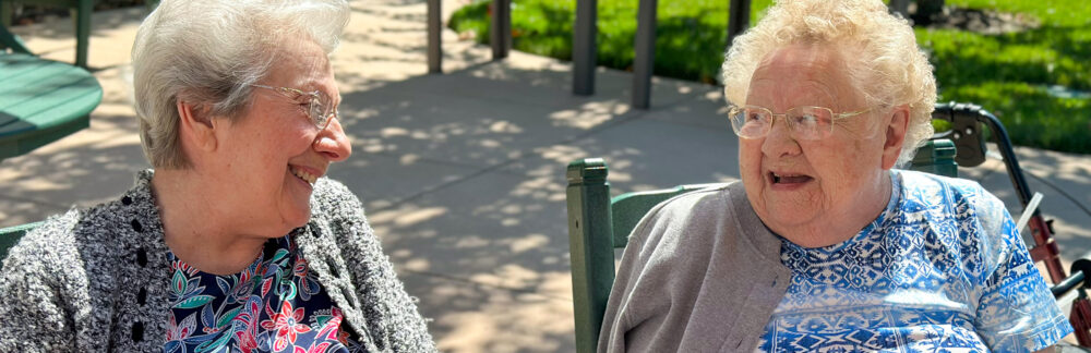 two older women are sitting in chairs talking to each other
