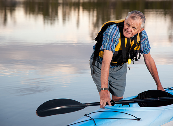 an elderly man wearing a life jacket is standing next to a blue kayak
