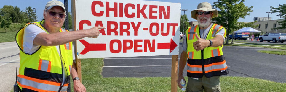 two men standing next to a sign that says chicken carry-out open