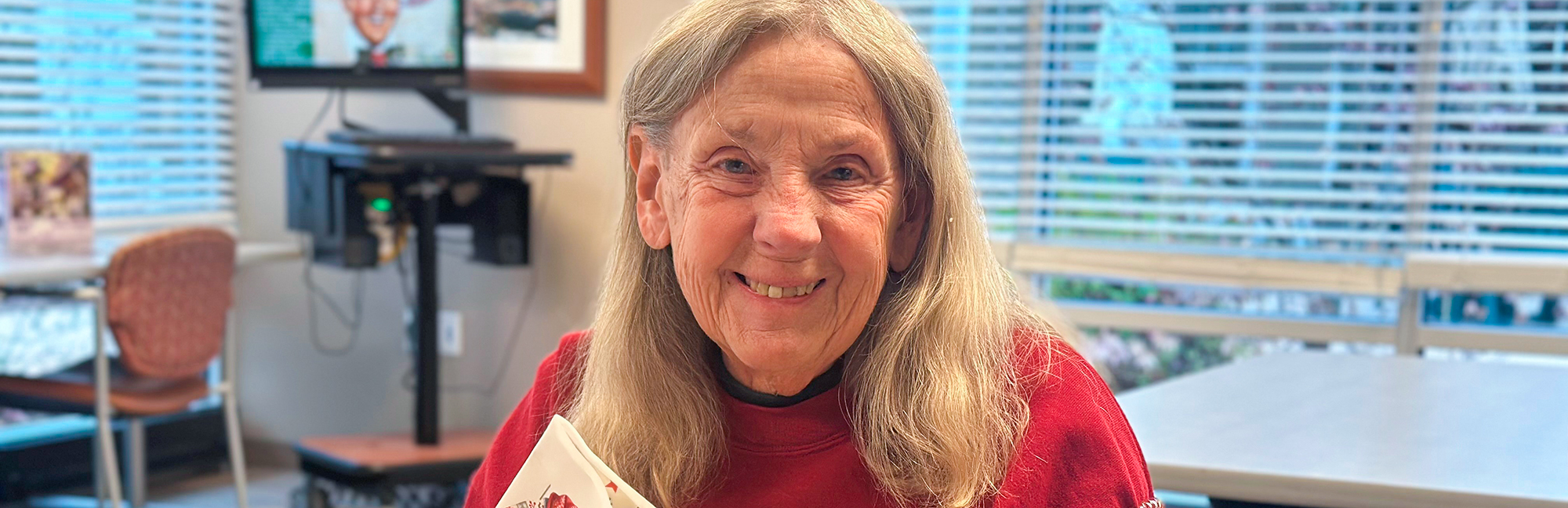 a happy elderly woman in a red sweater is smiling and holding a card